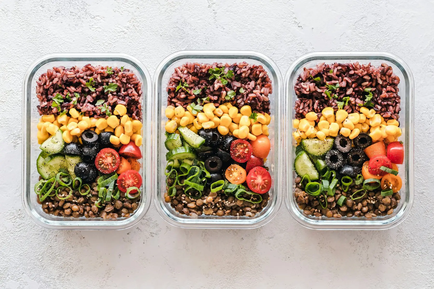 Três potes de vidro com refeições prontas: arroz, lentilha, milho, tomate, pepino e azeitona