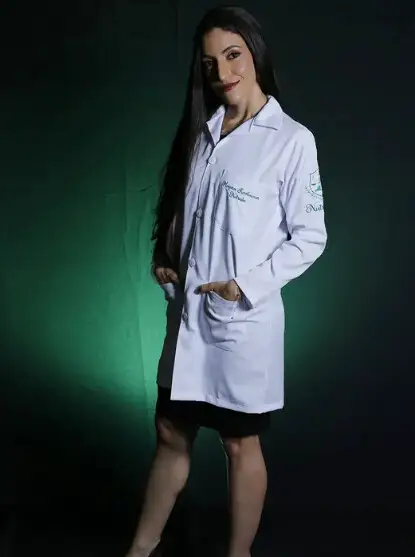 Mayara Kersbaumer de jaleco branco com o bordado "Nutricionista", diante de um fundo verde