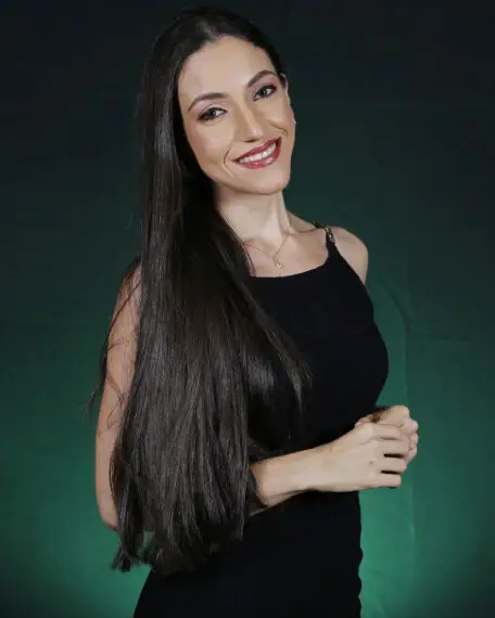 Mayara Kersbaumer de vestido preto, diante de um fundo verde
